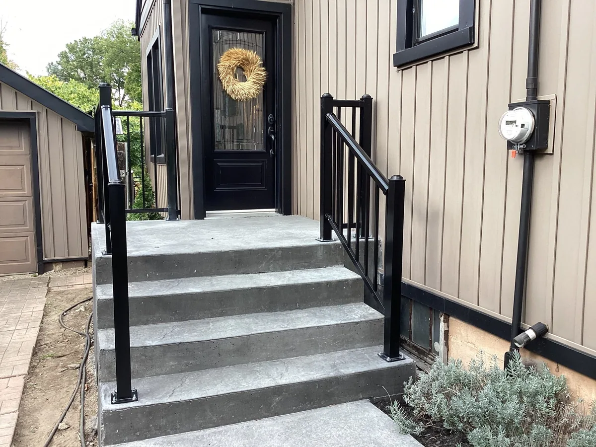 Concrete entry steps with black aluminum railings and modern exterior siding