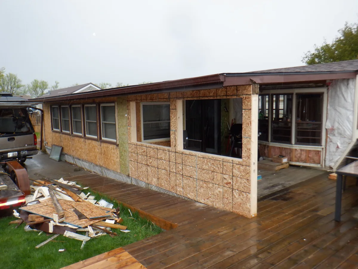 Cottage siding replacement in progress with house wrap and OSB sheathing