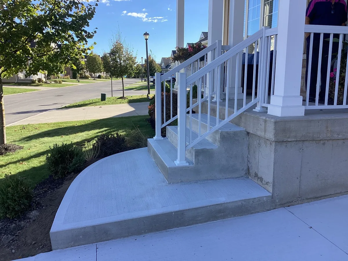 Poured concrete front porch with steps, curved walkway and white aluminum railings